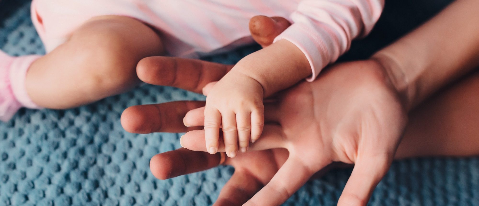 Auf zwei erwachsenen Händen liegt die kleine Hand eines Babys